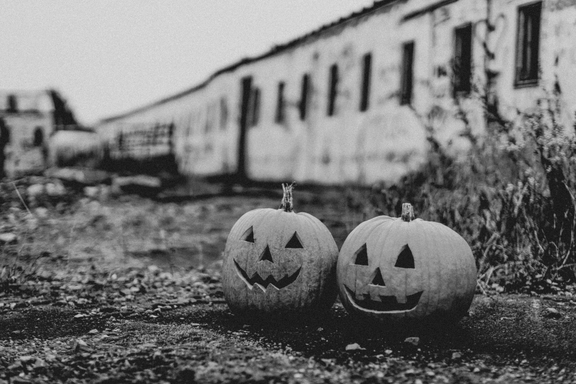 Two halloween pumpkins are sitting on the ground in front of a train.