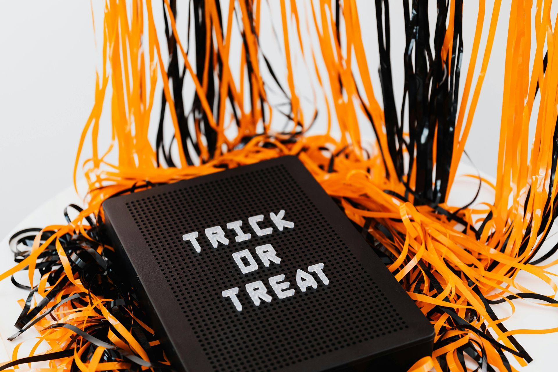 A trick or treat sign is sitting on top of a pile of orange and black tinsel.