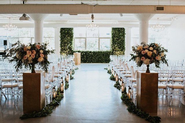 A wedding ceremony is taking place in a large room with chairs and flowers.