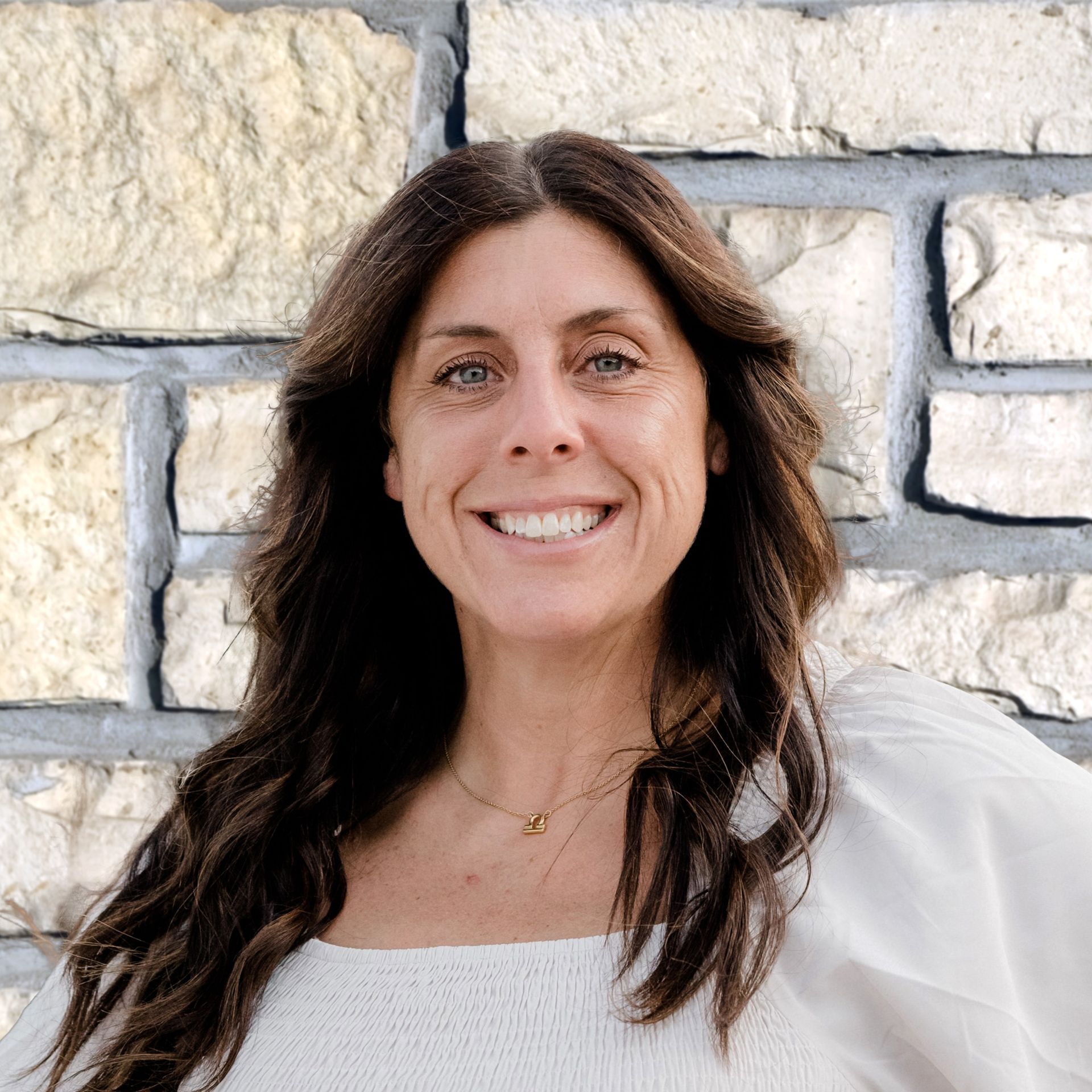 A woman is smiling in front of a brick wall.