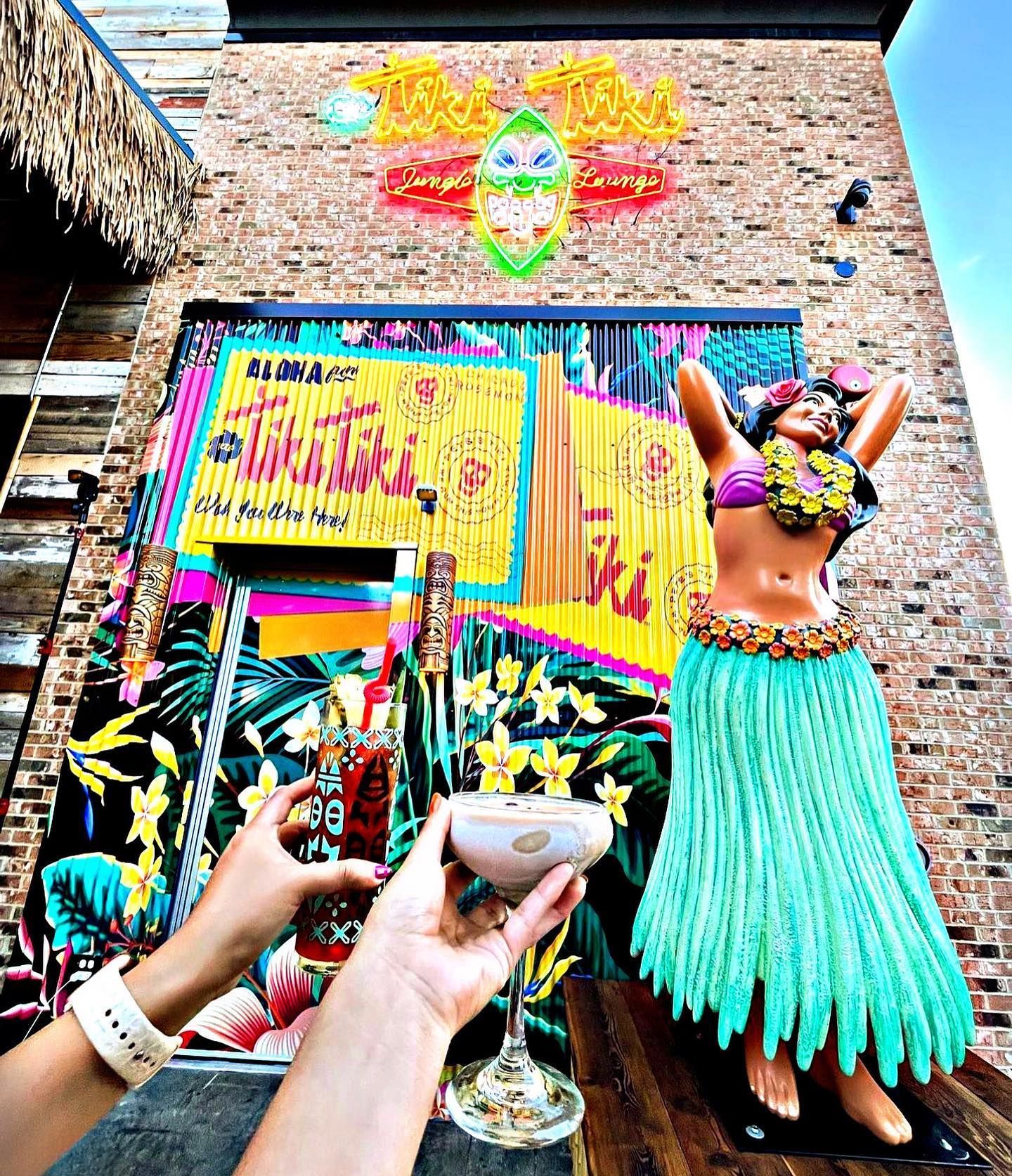A person is holding a drink in front of a tiki statue