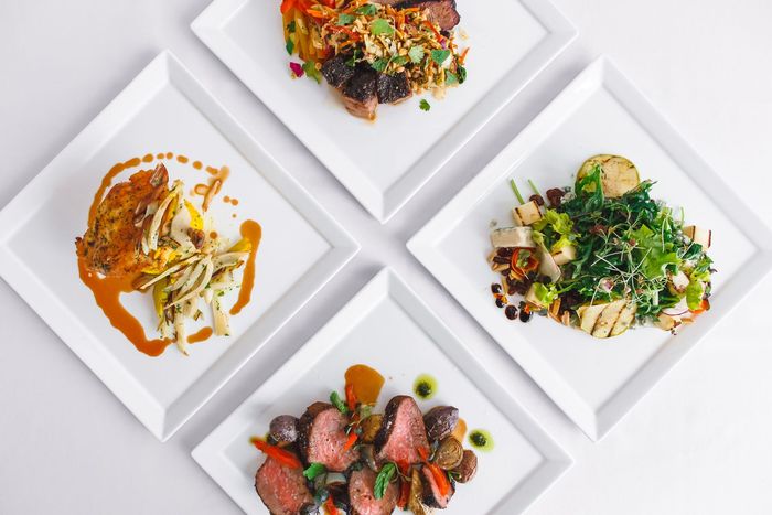 A white plate topped with skewers of meat and vegetables next to a plant.