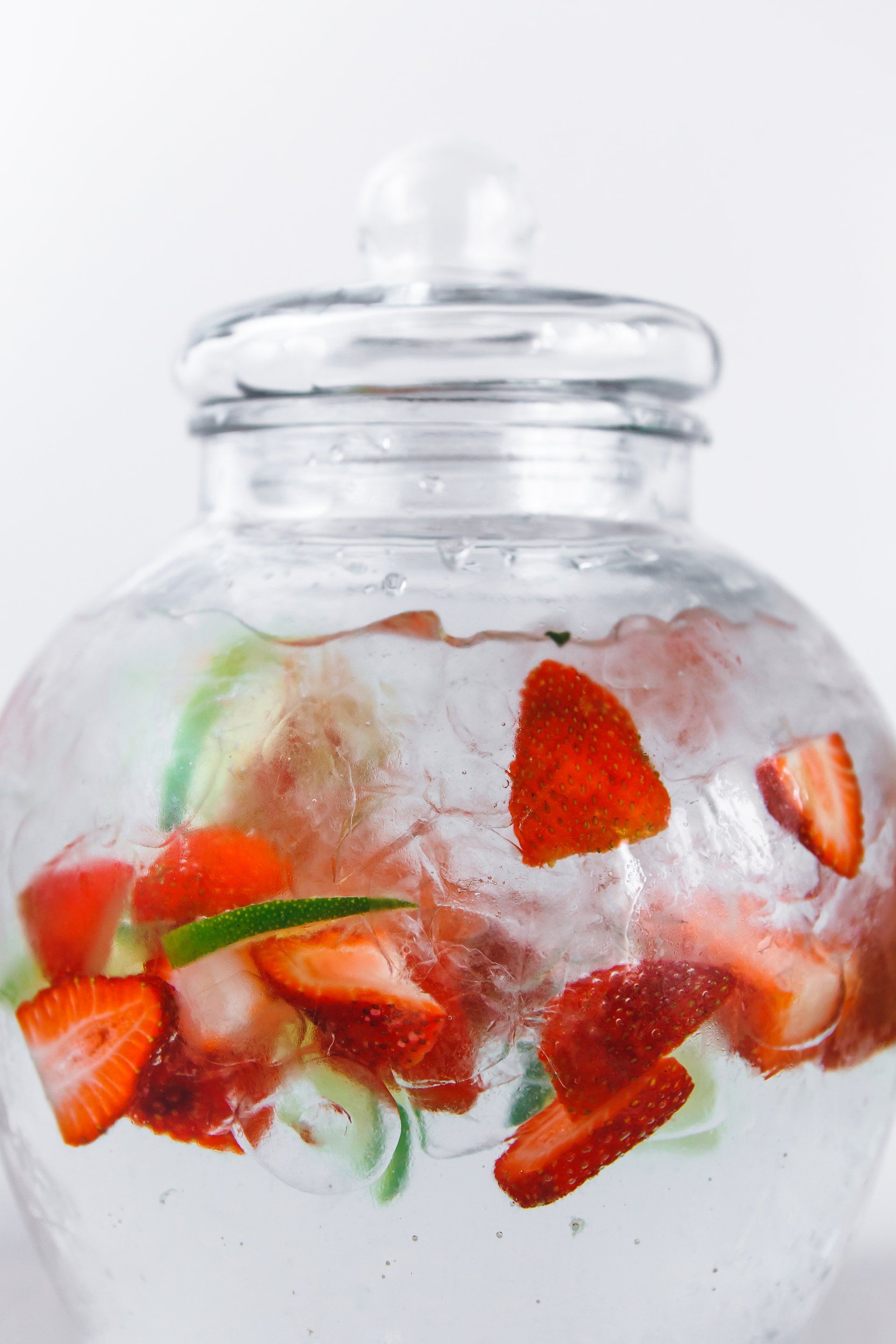 Strawberries and cucumber are in a glass jar of water.