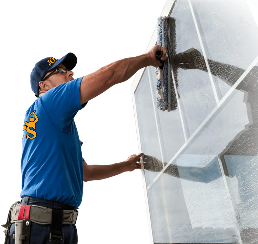 Window washer in blue shirt and hat, cleaning a large, geometric window with a squeegee.