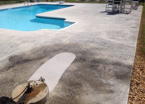 A concrete patio with a swimming pool in the background being cleaned at an affordable price
