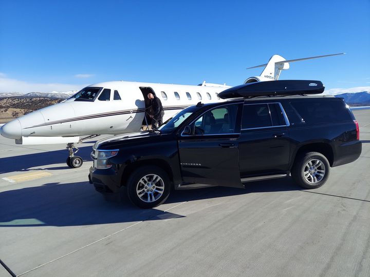 A black suv is parked in front of a private jet