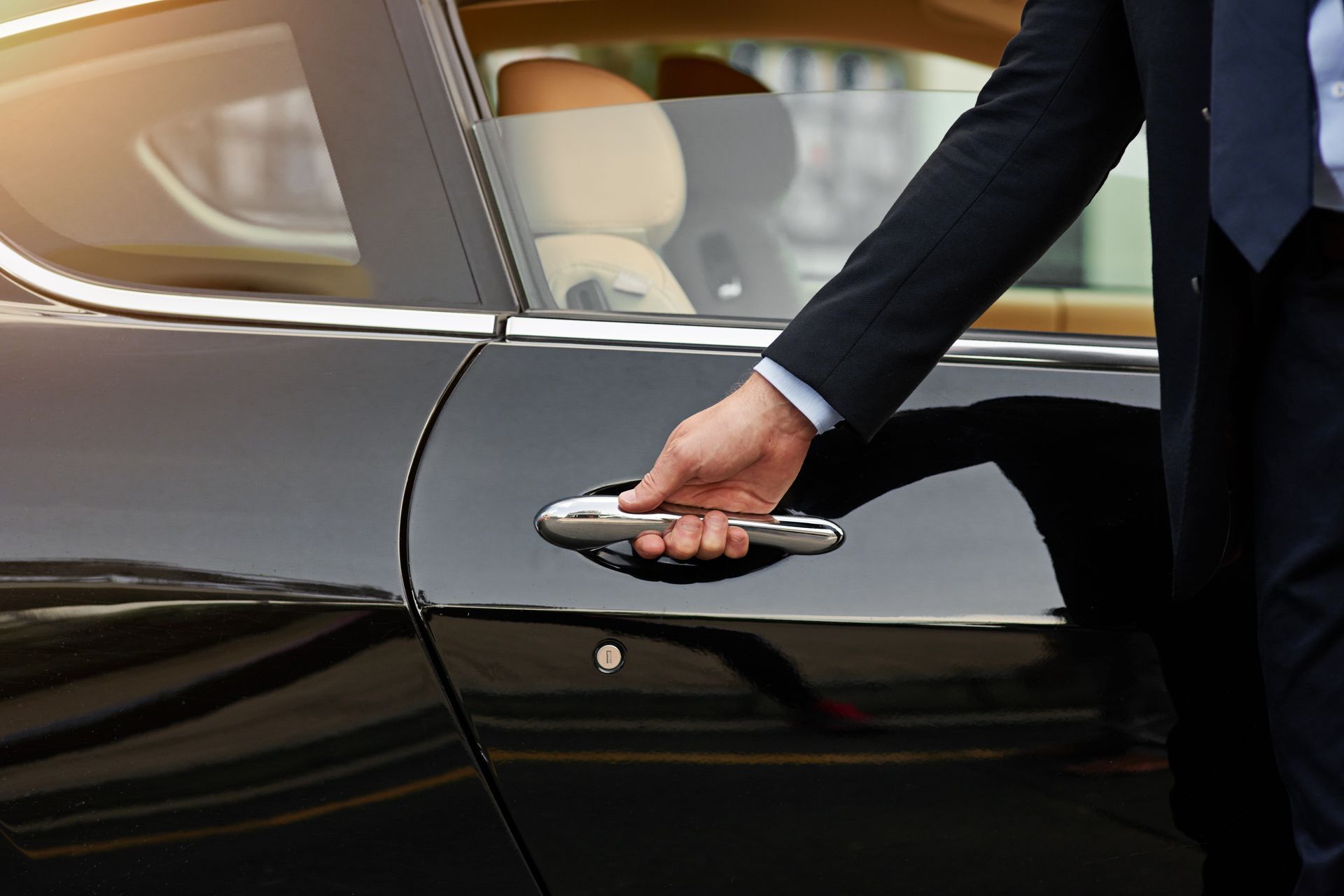 A man in a suit is opening the door of a black car.