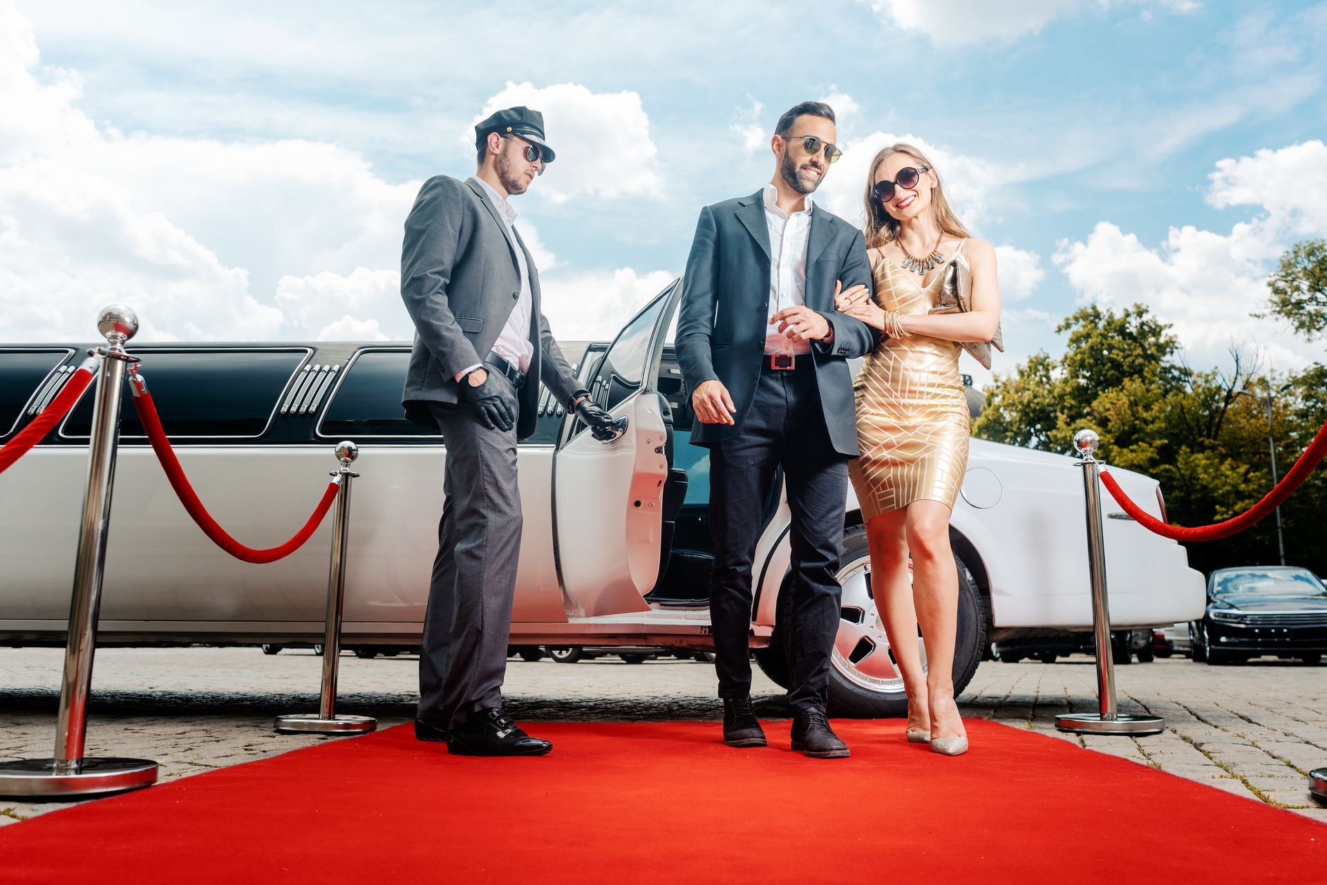 A man and a woman are standing on a red carpet in front of a limousine.