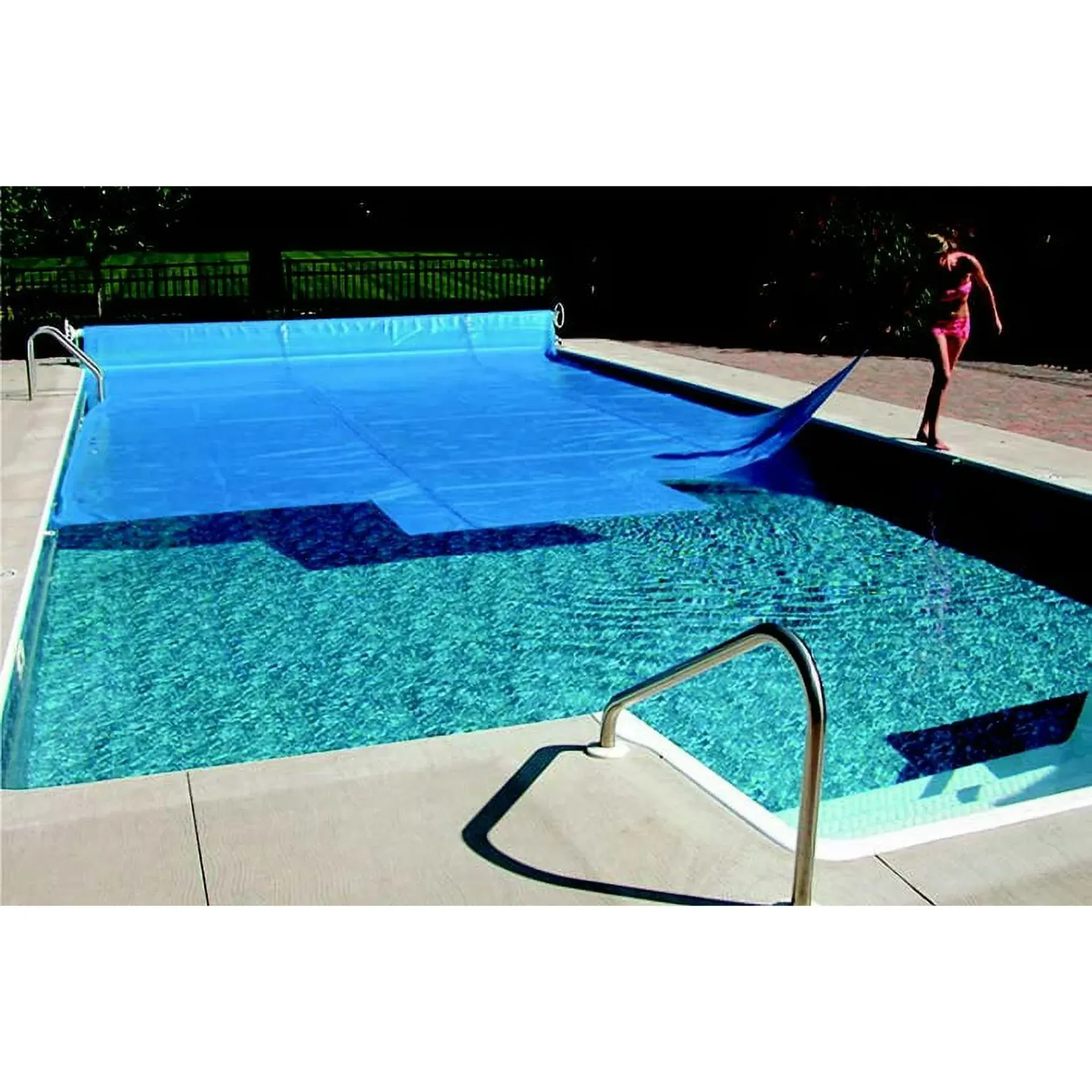 A woman is standing on the edge of a swimming pool with a blue cover on it.