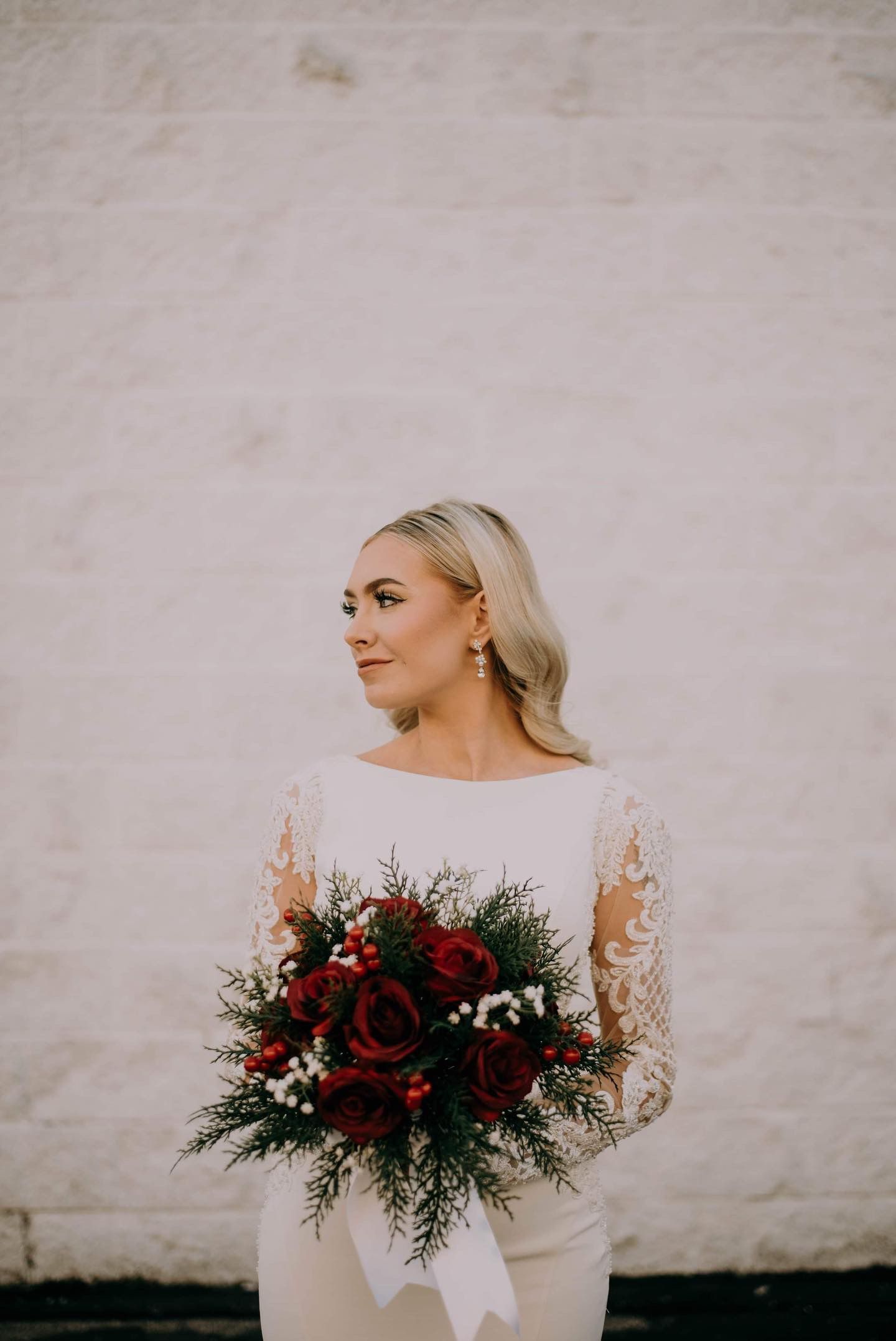 A bride in a white dress is holding a bouquet of red flowers.