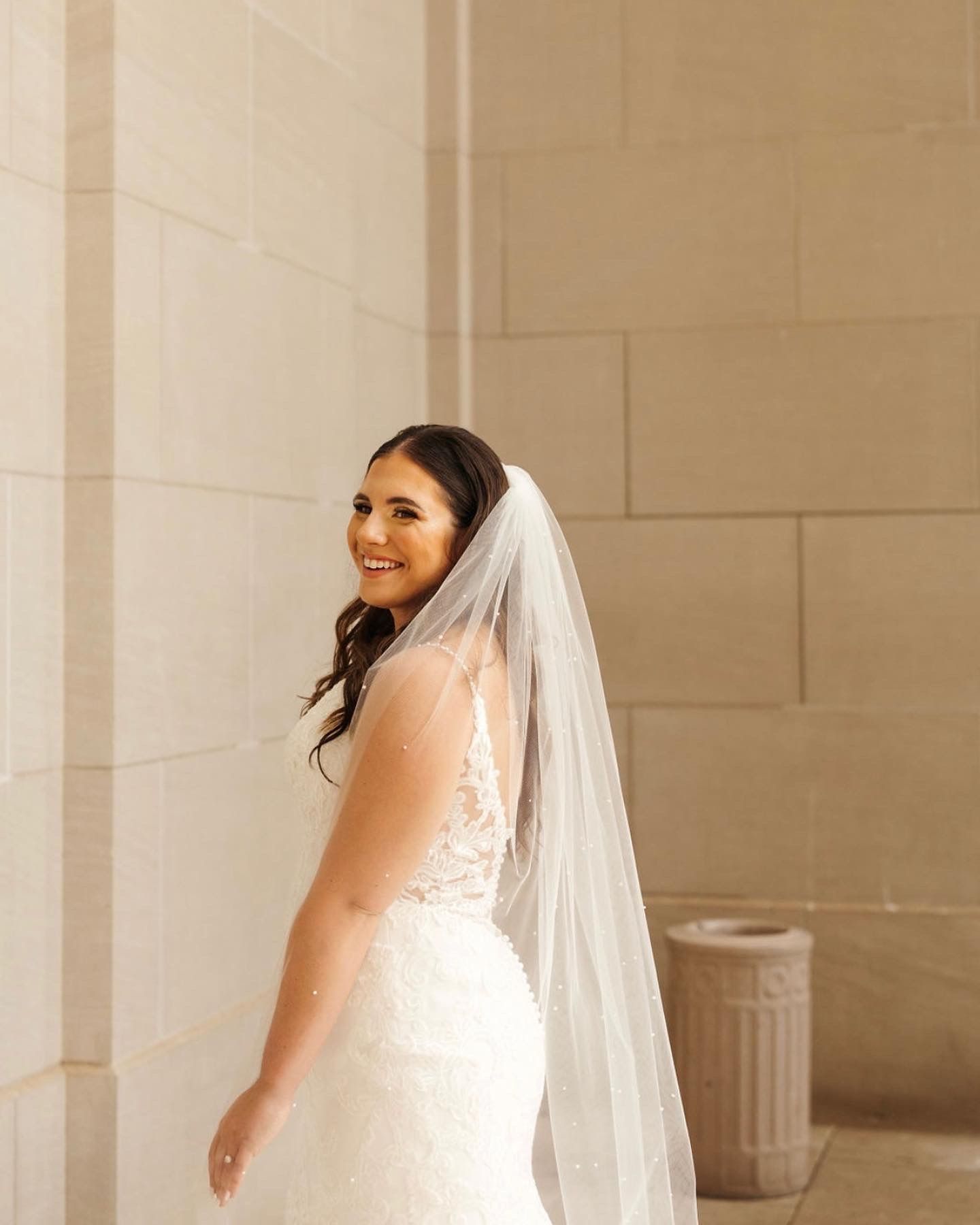 A woman in a wedding dress and veil is standing in front of a wall.