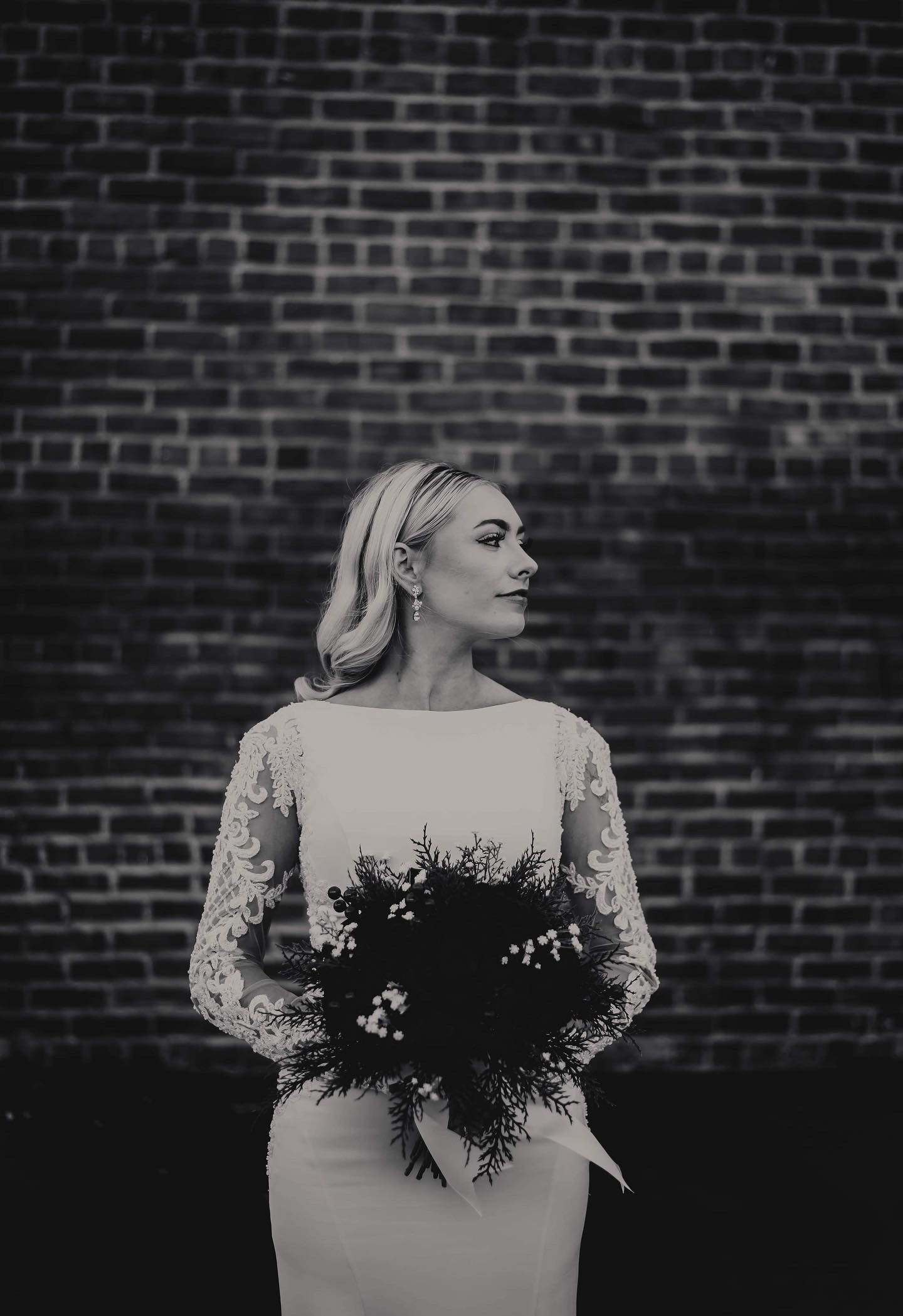 A bride in a wedding dress is standing in front of a brick wall holding a bouquet of flowers.