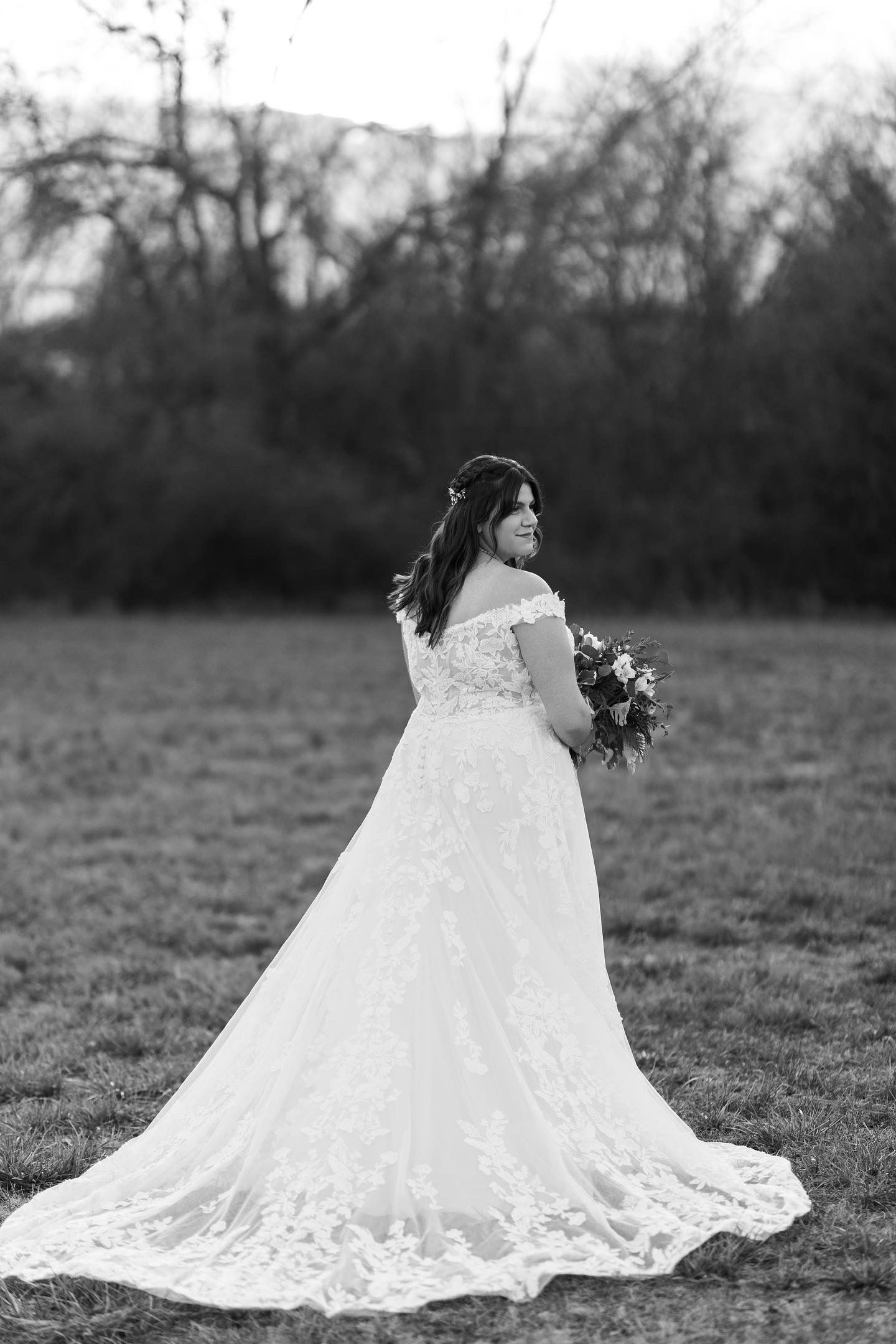 A bride in a wedding dress is standing in a field holding a bouquet of flowers.