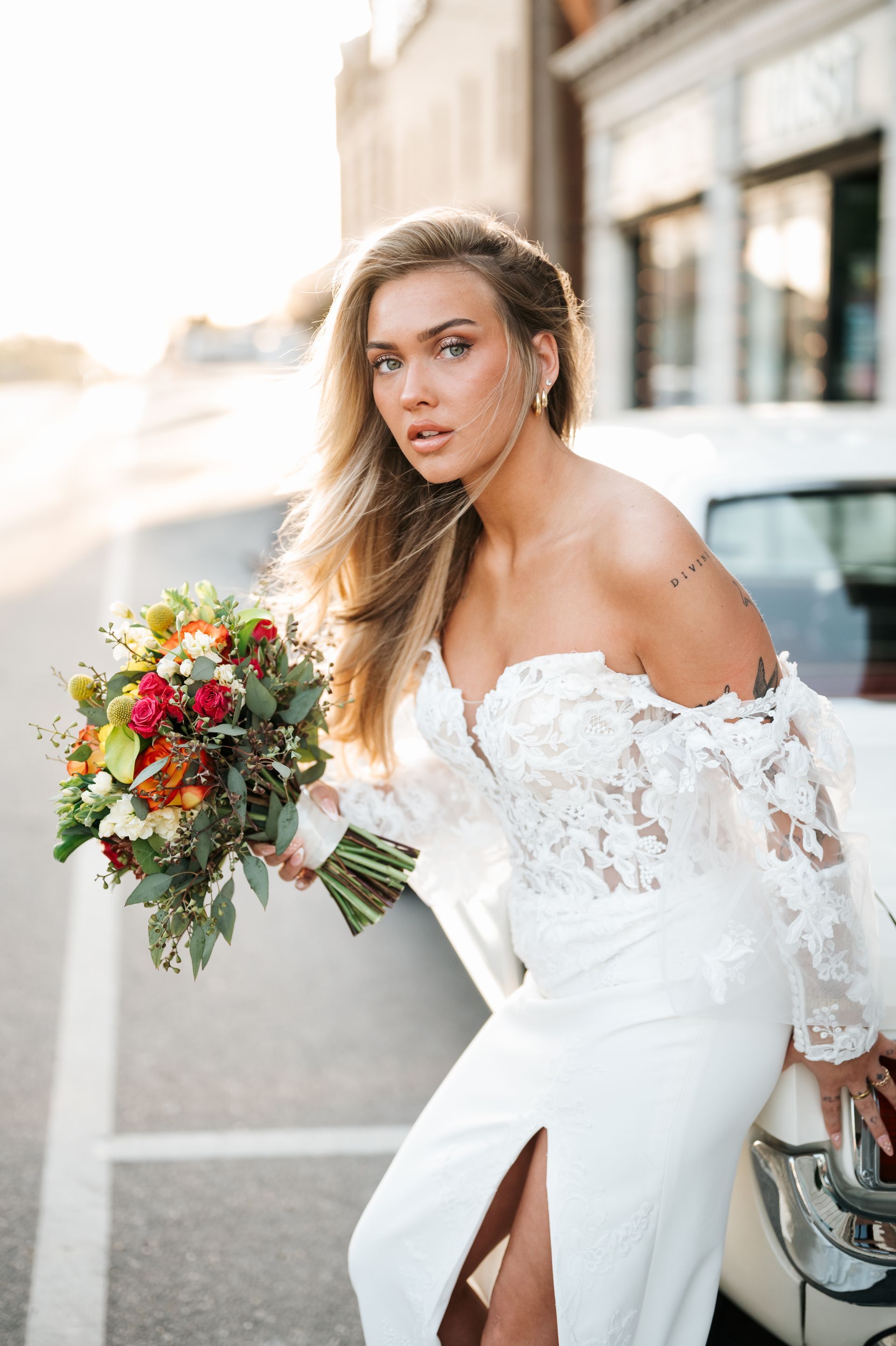 A woman in a wedding dress with a high slit is standing in front of palm trees.