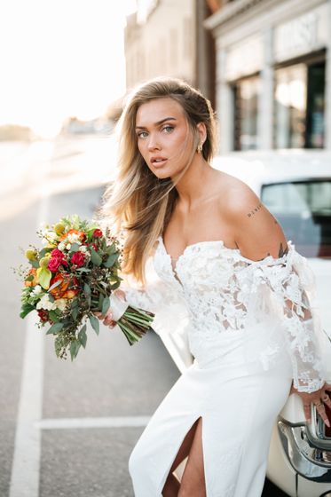 A woman in a wedding dress with a high slit is standing in front of palm trees.