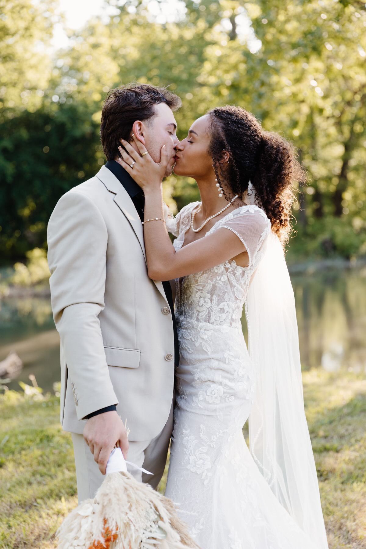 A bride and groom are kissing in front of a lake.