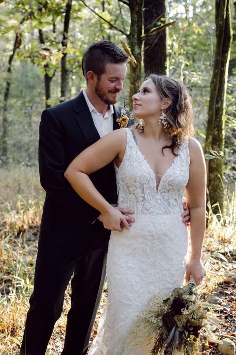 A bride and groom are posing for a picture in the woods.