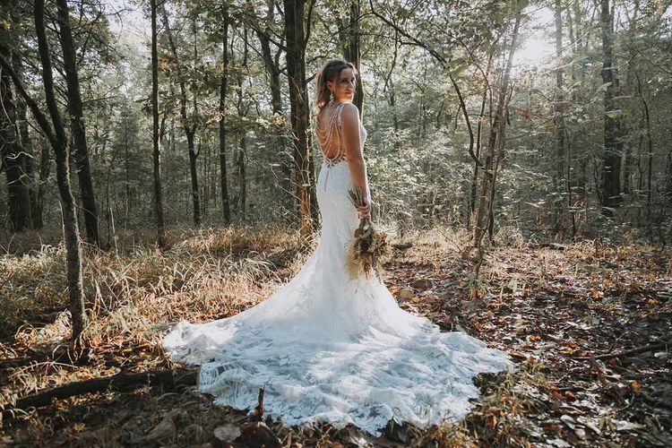 A bride in a wedding dress is standing in the middle of a forest.