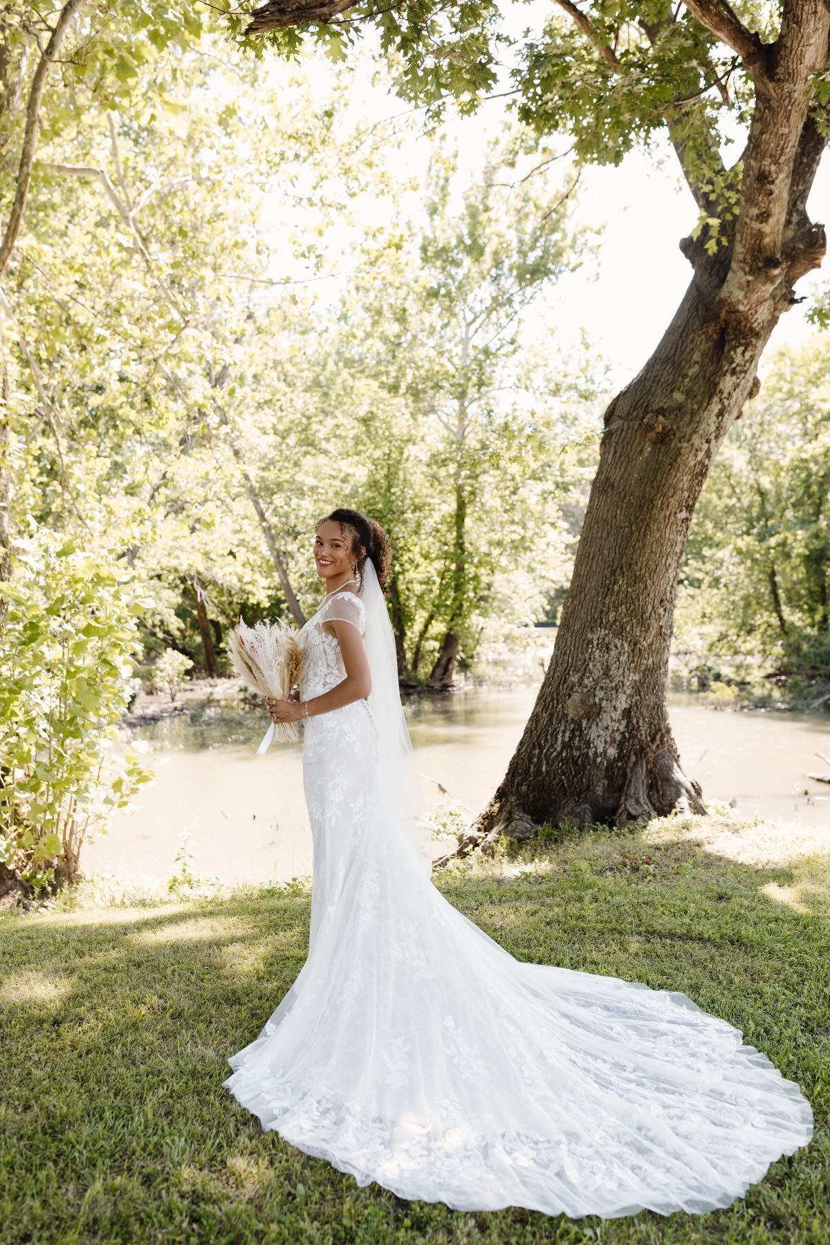 A bride in a wedding dress is standing in front of a tree holding a bouquet of flowers.