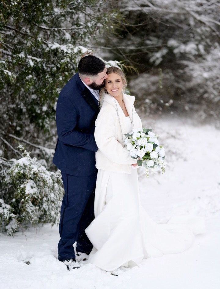 A bride and groom are posing for a picture in the snow.