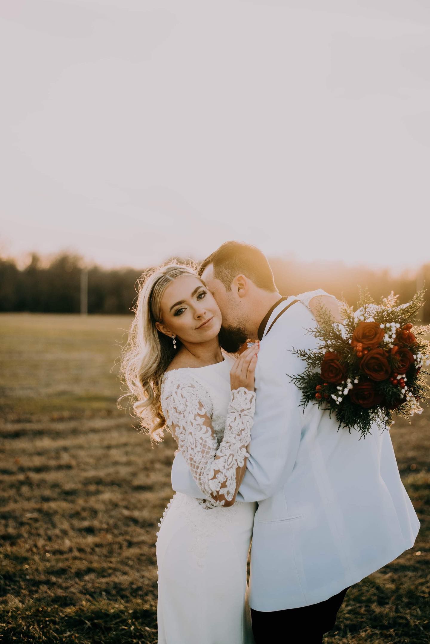 A bride and groom are kissing in a field at their wedding.