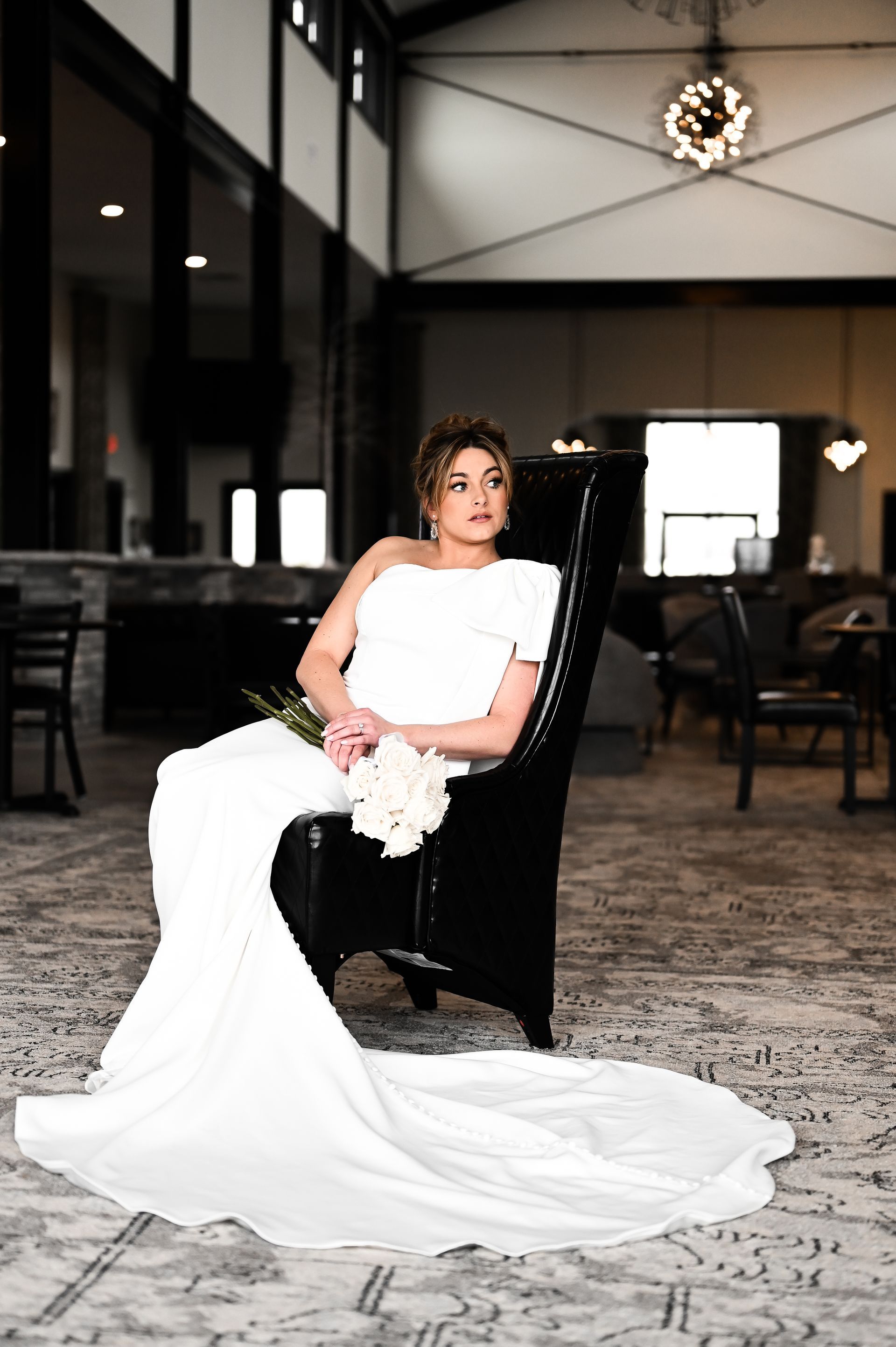 A bride in a white dress is sitting in a chair holding a bouquet of flowers.