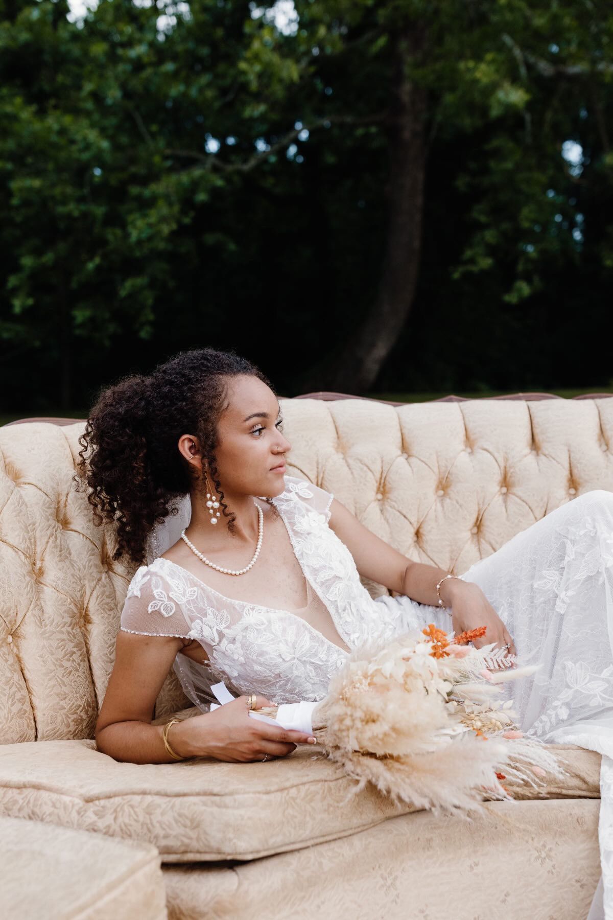 A woman in a wedding dress is sitting on a couch holding a bouquet of flowers.