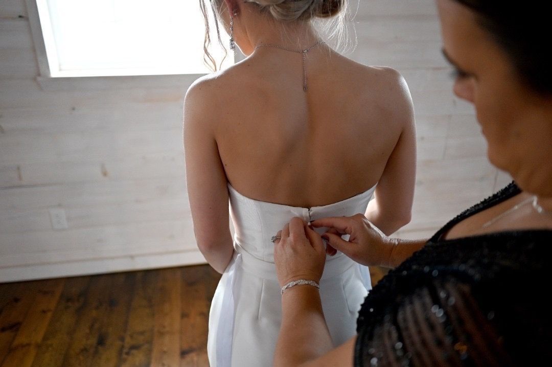 A woman is helping a bride with her wedding dress.