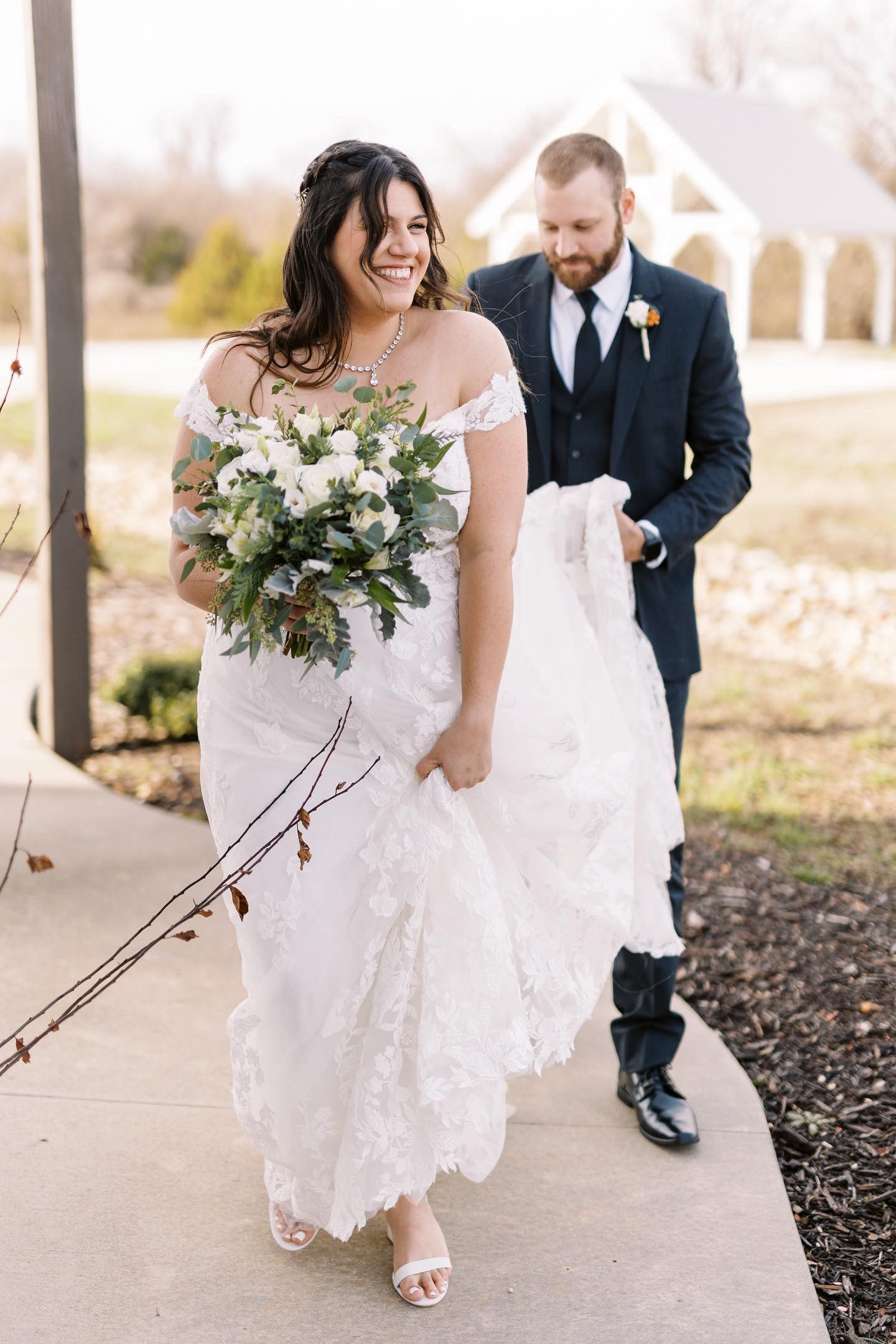 A bride and groom are walking down a sidewalk . the bride is holding a bouquet of flowers.