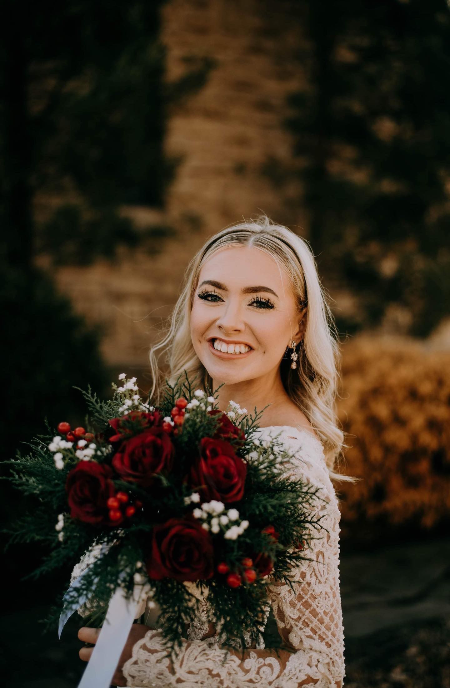 A bride is smiling while holding a bouquet of red roses.