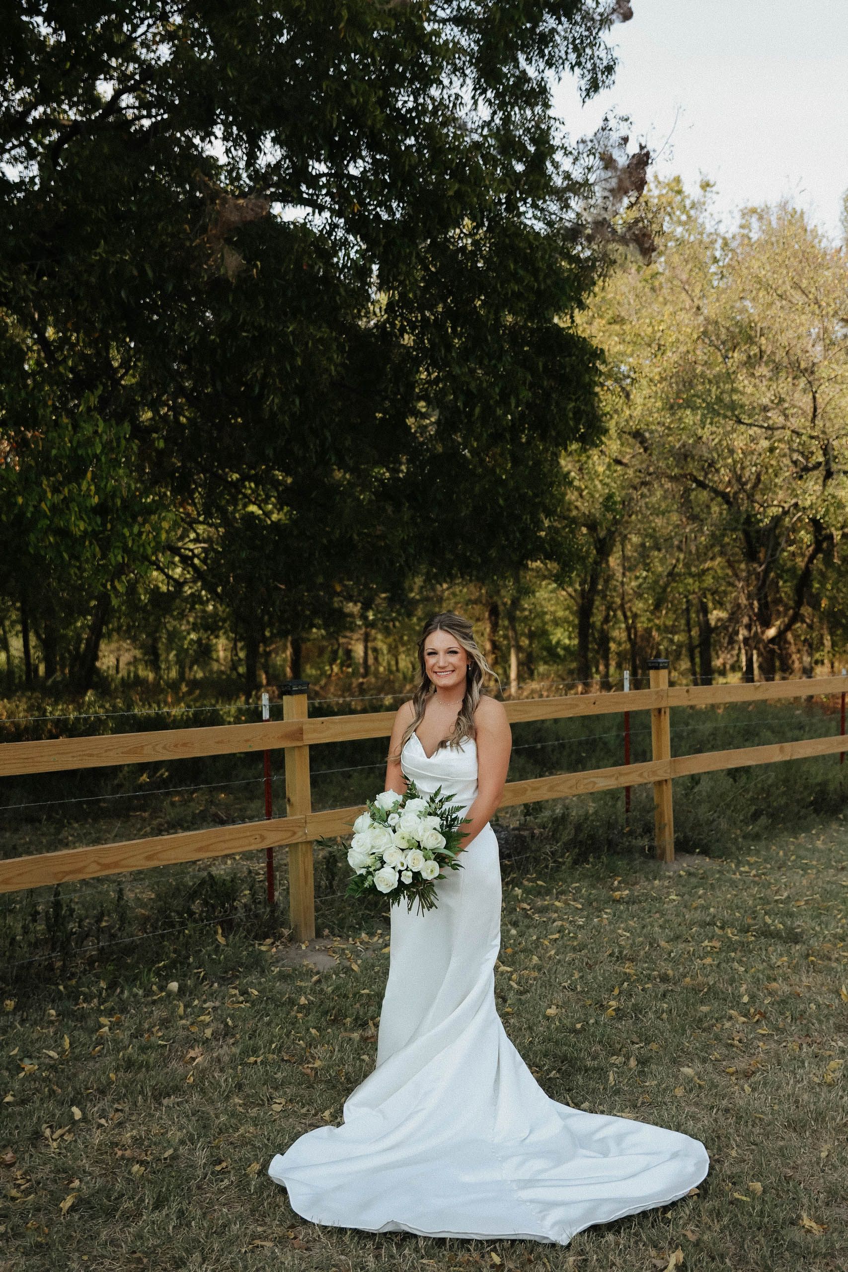 A bride in a wedding dress is standing in a field holding a bouquet of flowers.