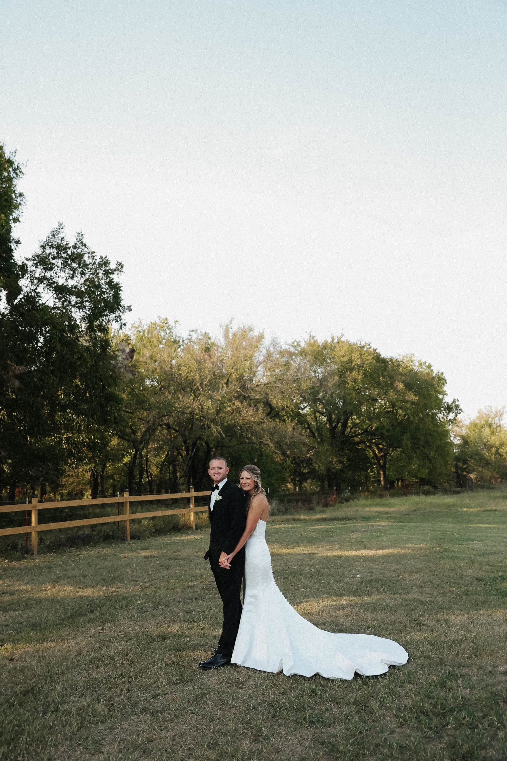 A bride and groom are standing in a field holding hands.