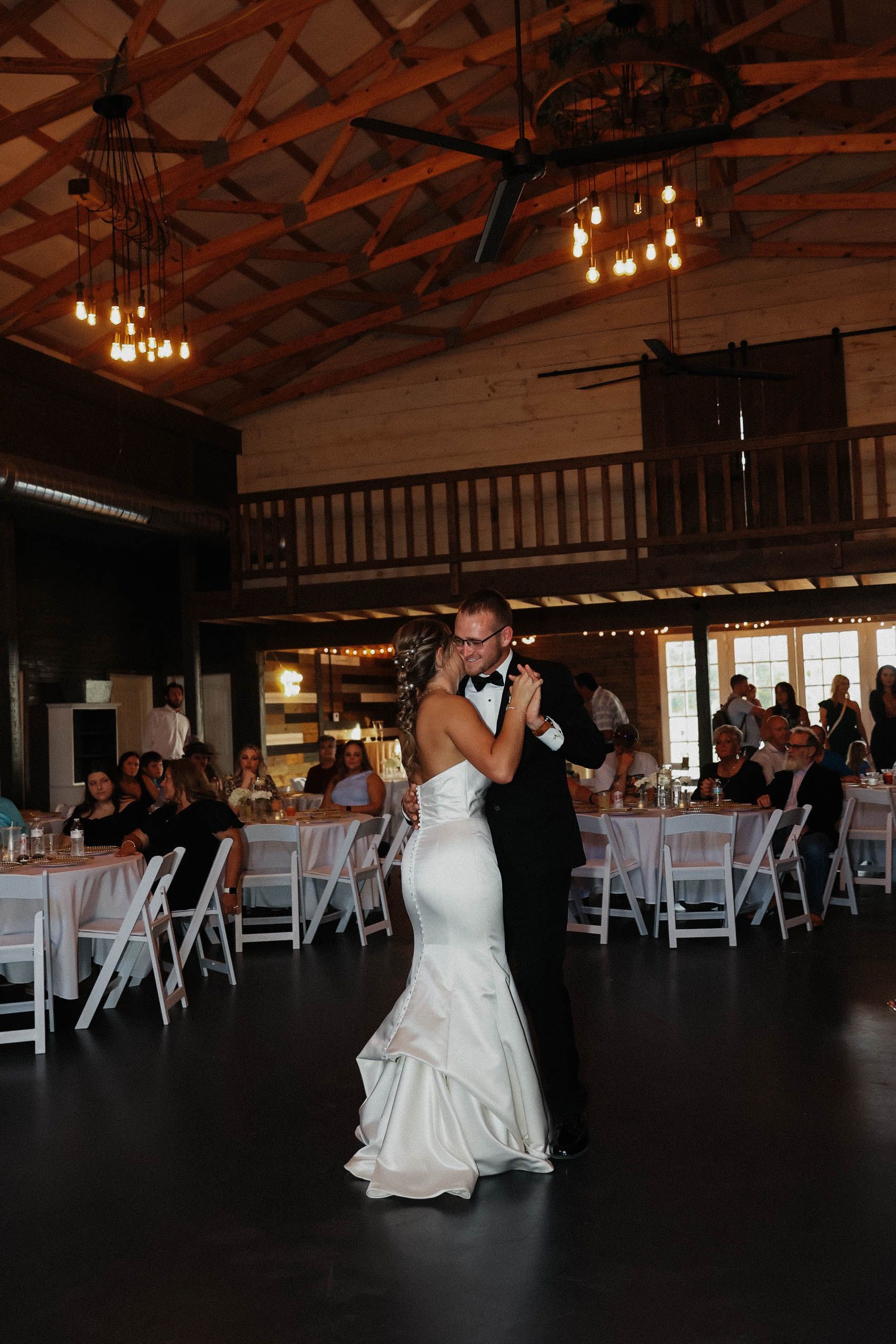 A bride and groom are dancing in a large room at their wedding reception.