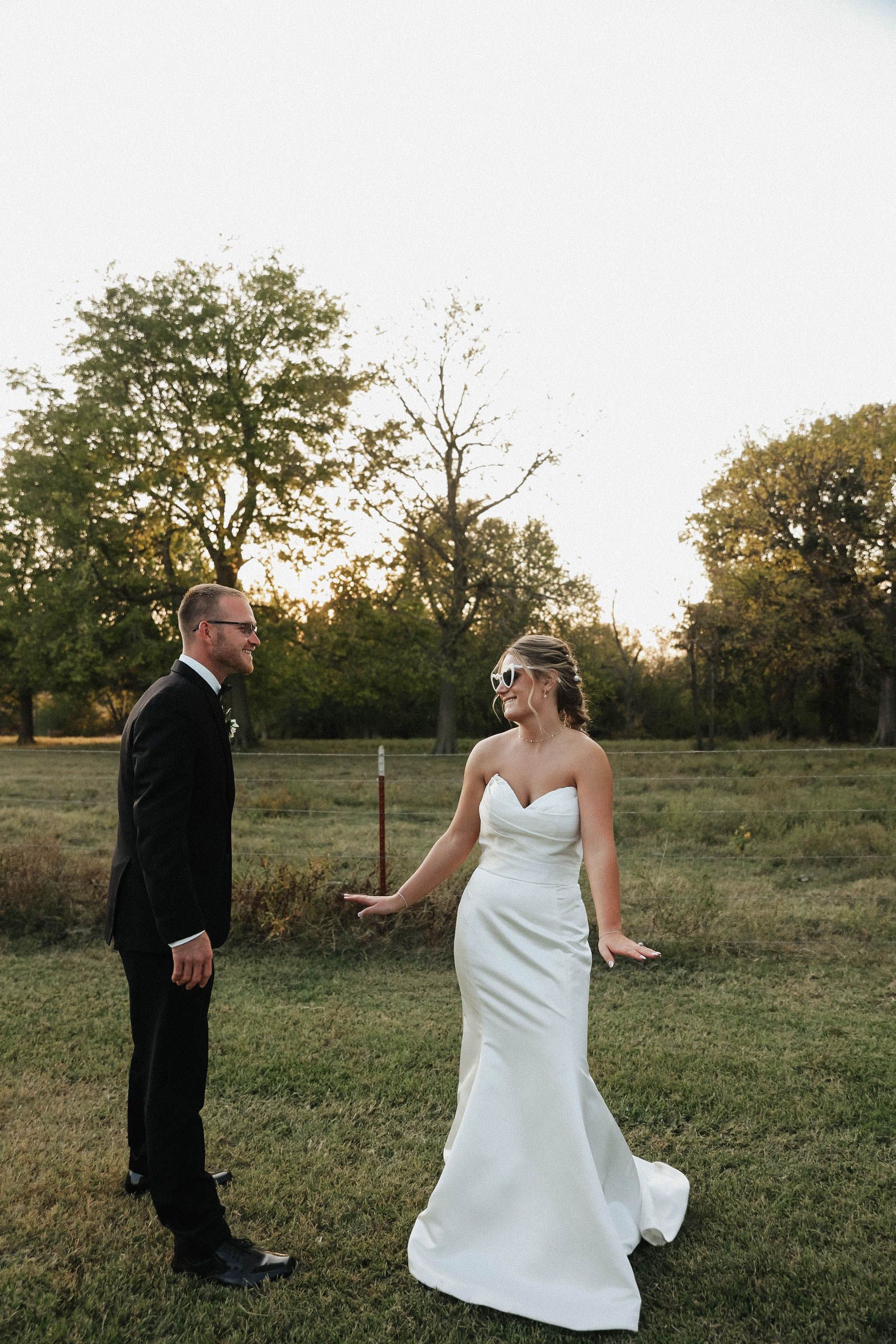 A bride and groom are standing in a field holding hands.