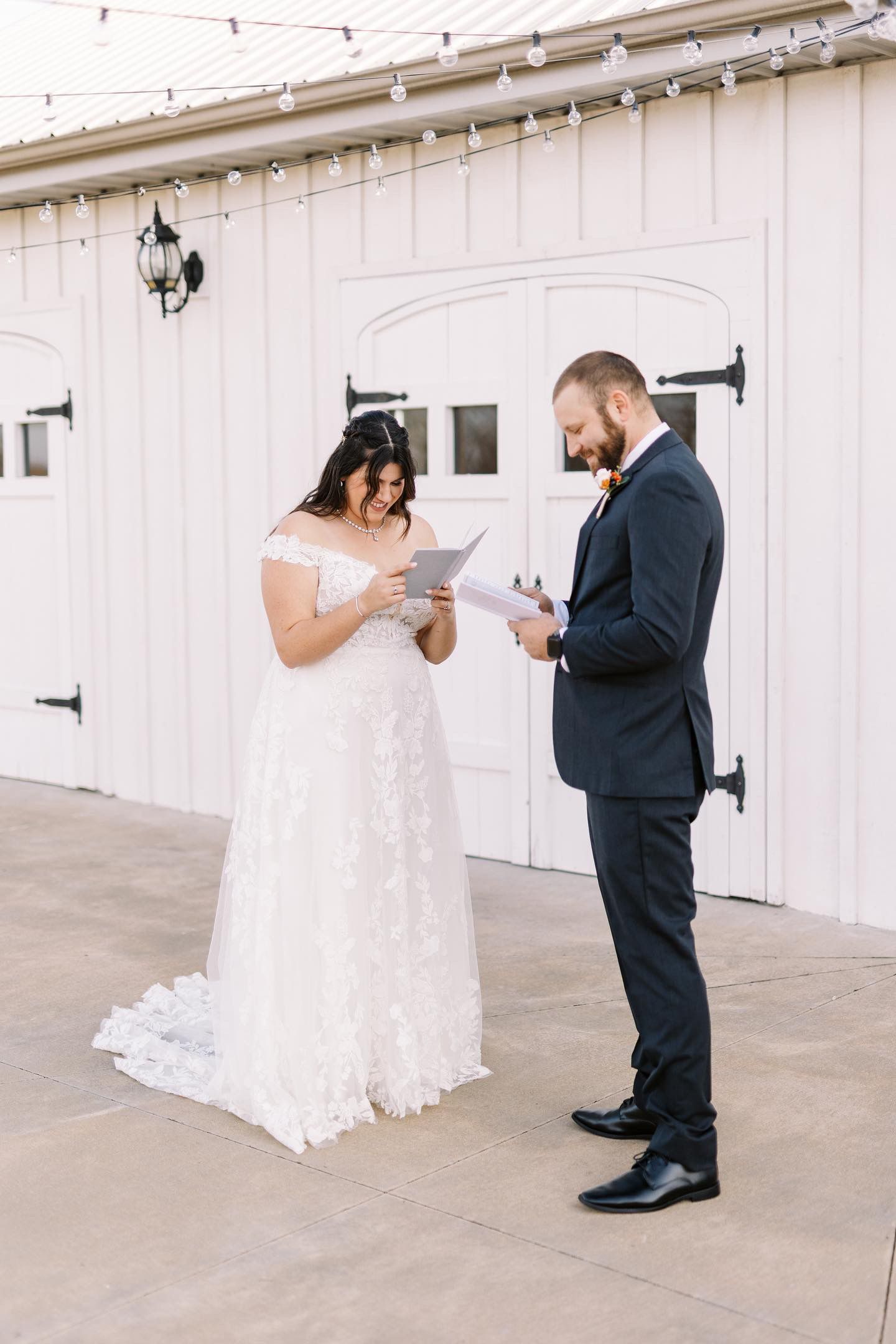 A bride and groom are reading their wedding vows in front of a white barn.