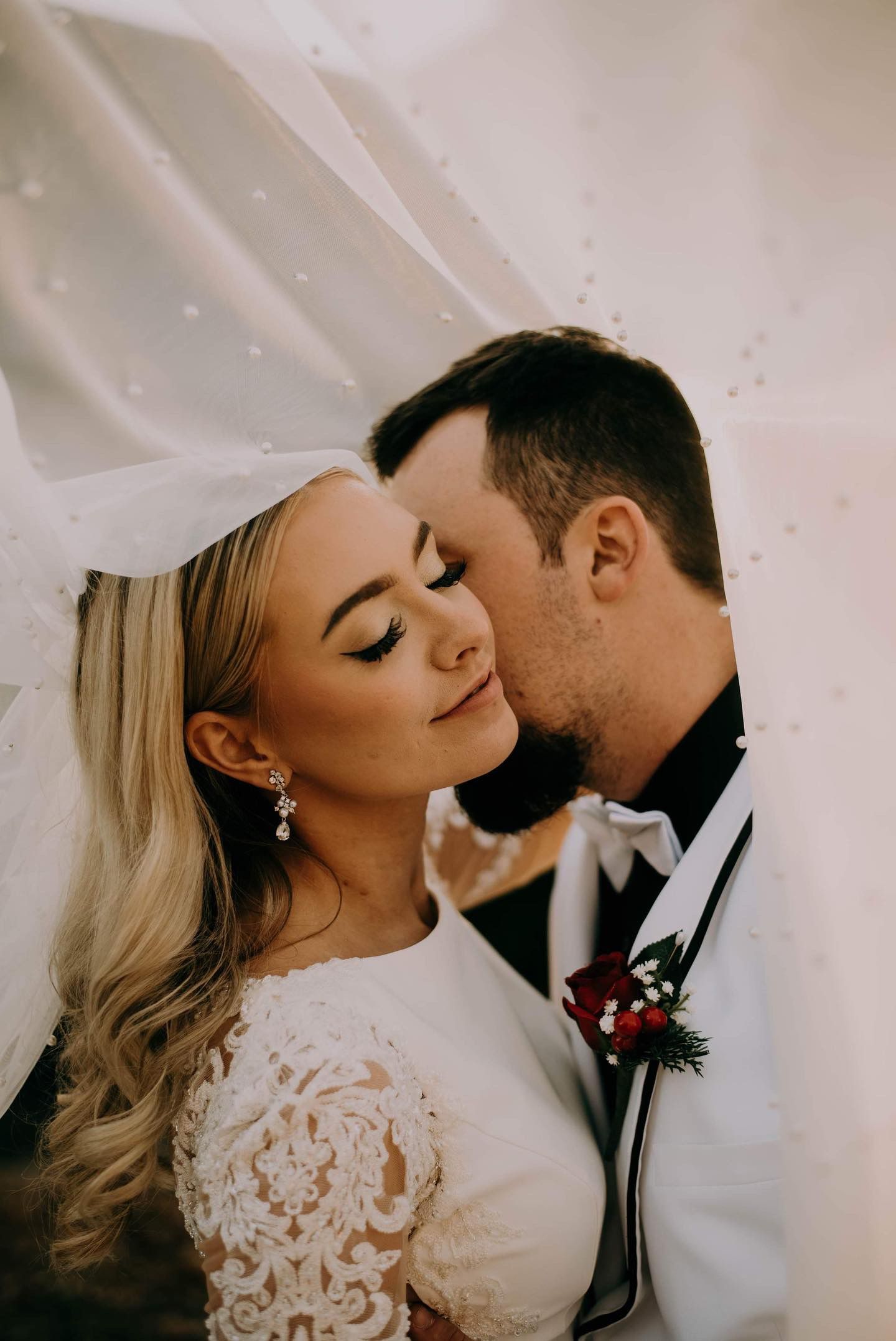 A bride and groom are kissing under a veil.