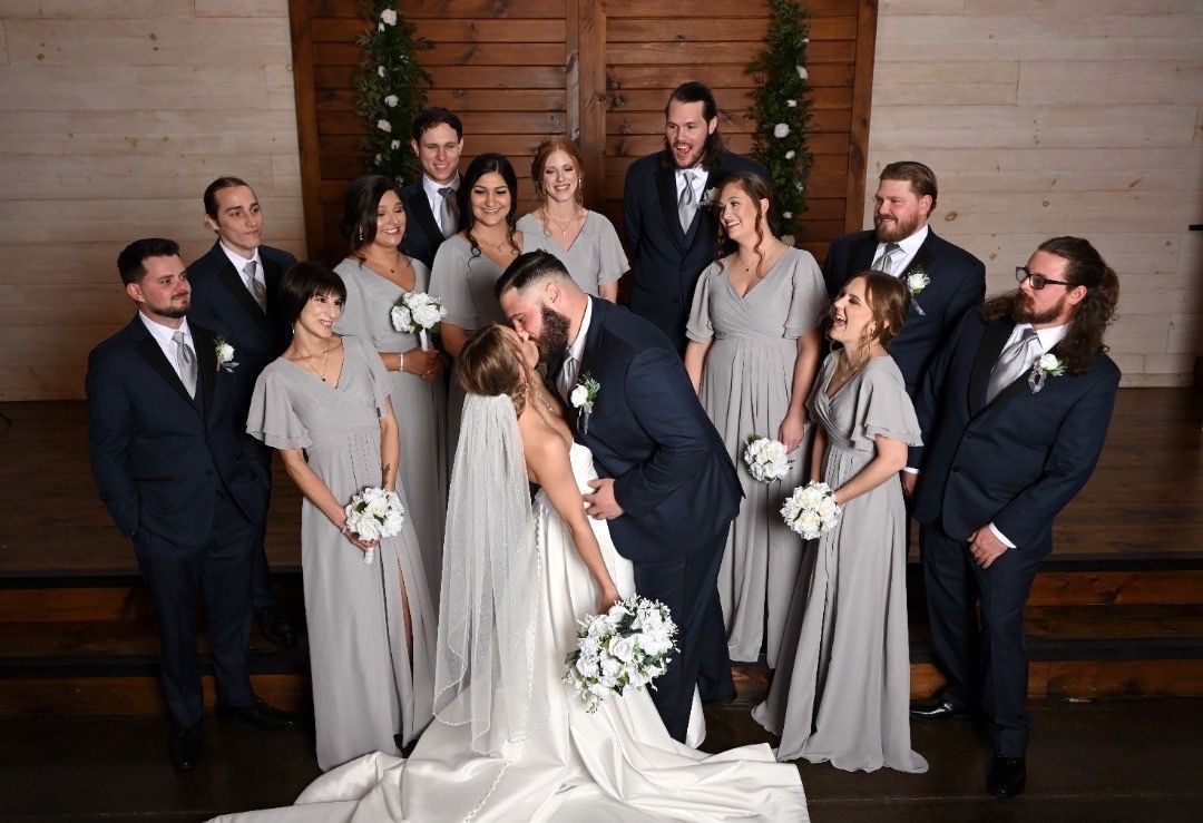 A bride and groom are kissing in front of their wedding party.
