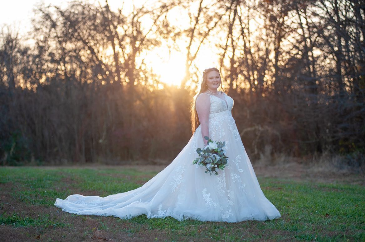 A bride in a wedding dress is standing in a field holding a bouquet of flowers.