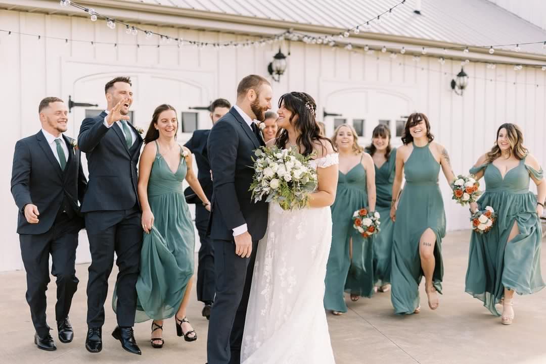 A bride and groom are kissing while walking with their wedding party.