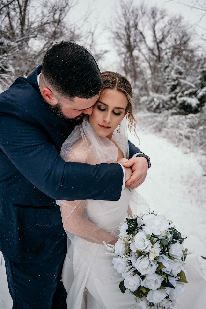 A bride and groom are posing for a picture in the snow.