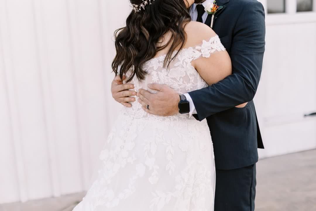 A bride and groom are hugging each other in front of a white building.