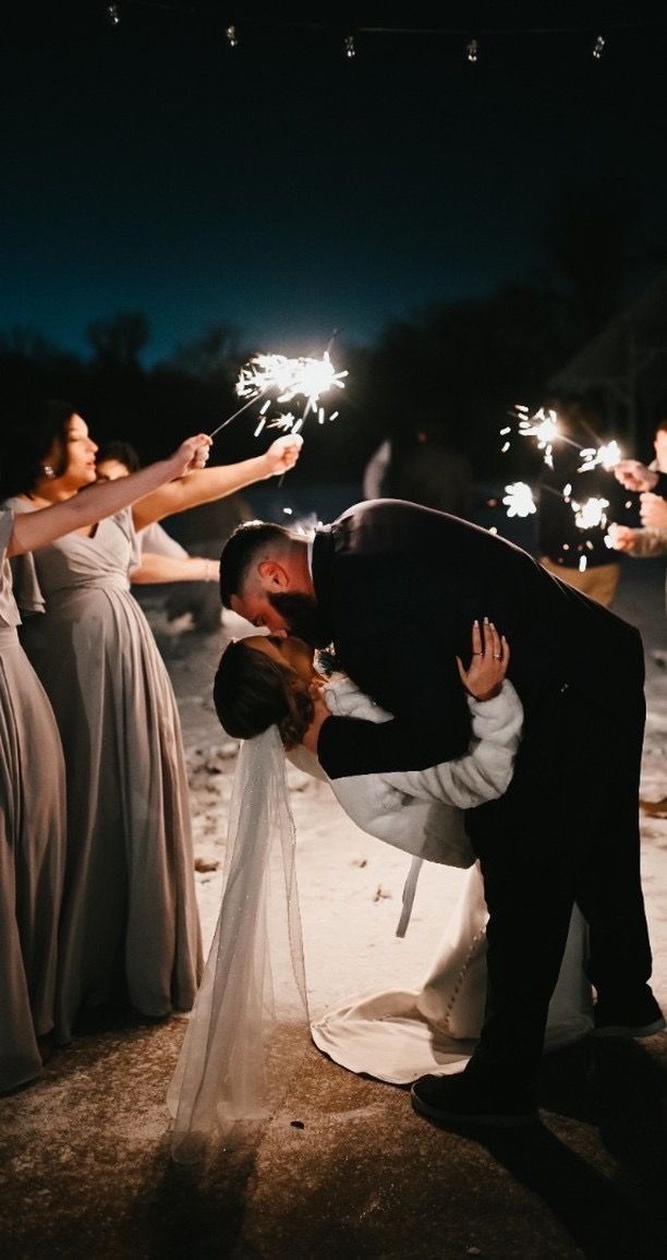 A bride and groom kissing while holding sparklers at their wedding reception.