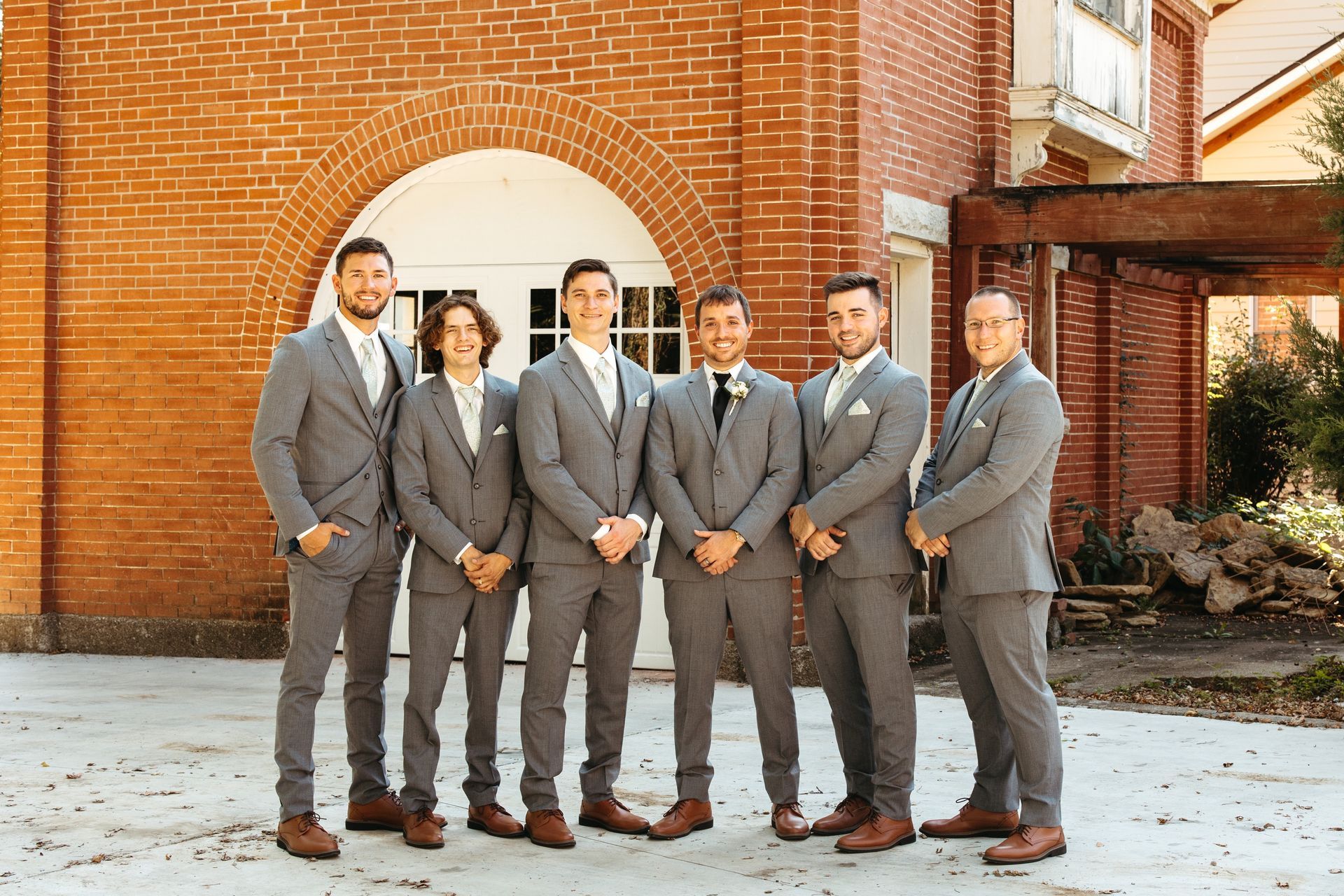 A group of men in suits are posing for a picture in front of a brick building.