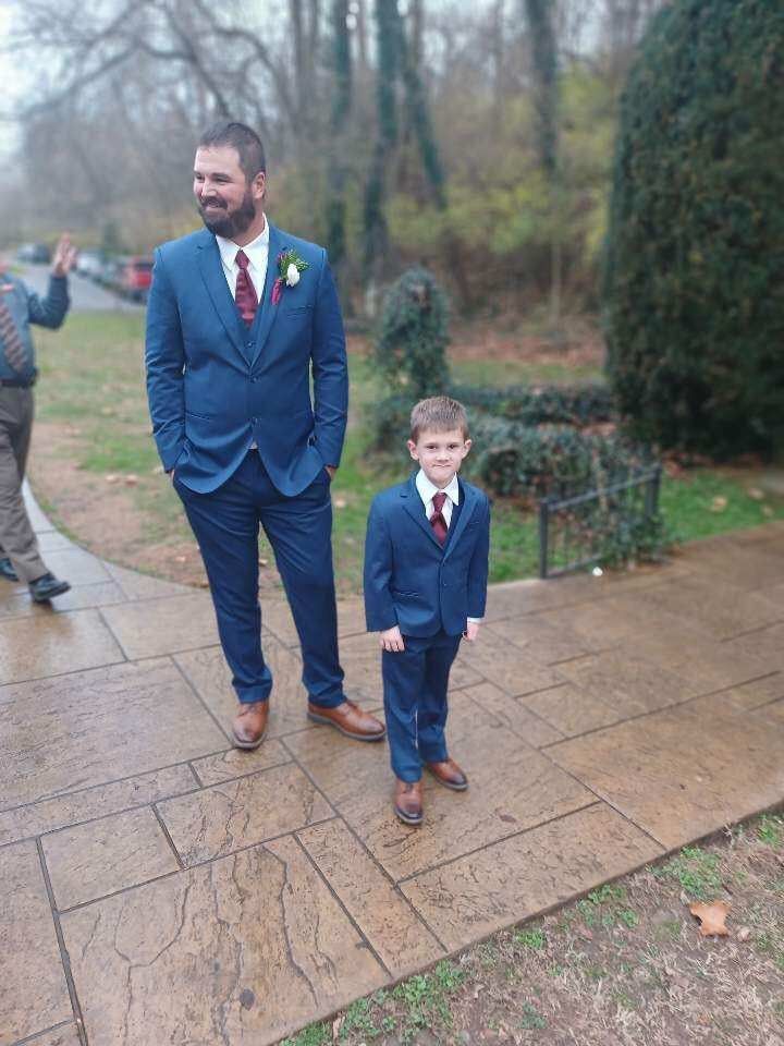 A man and a boy in suits are standing next to each other on a sidewalk.