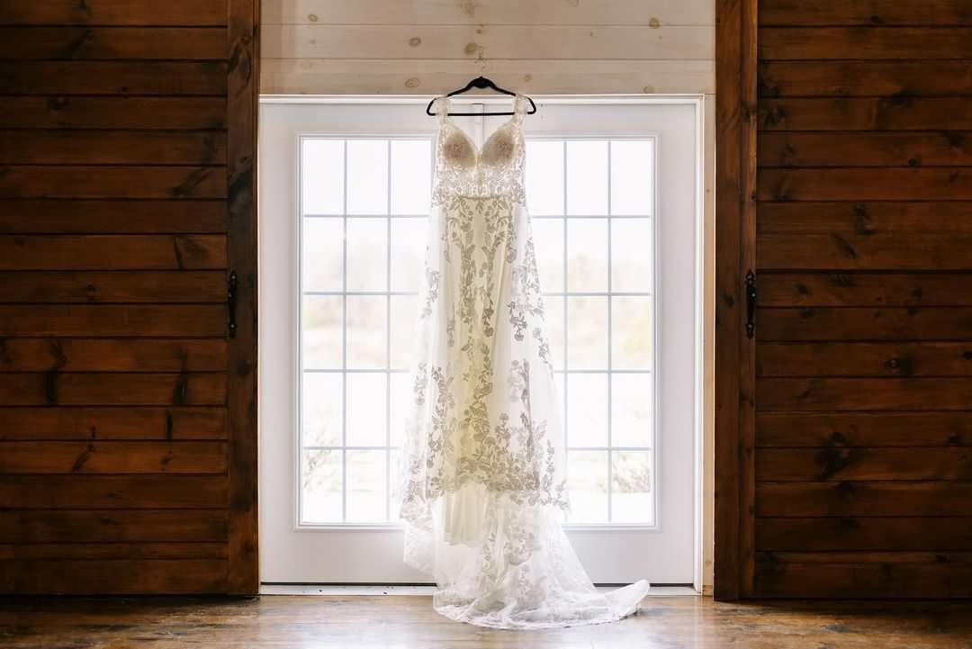 A wedding dress is hanging on a hanger in front of a window.