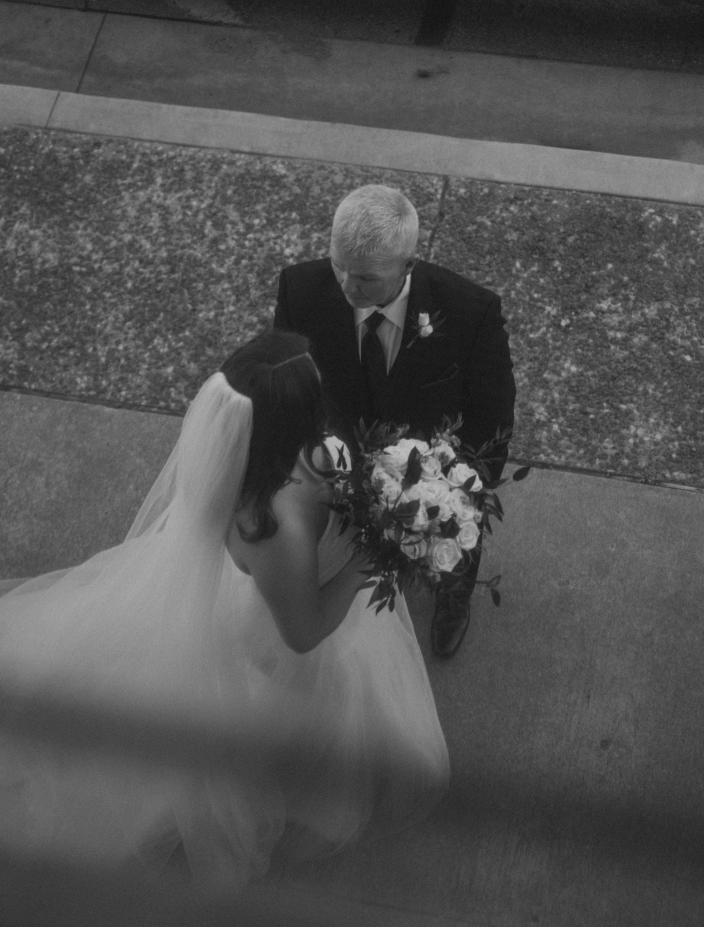 A black and white photo of a bride and her father walking down the aisle.