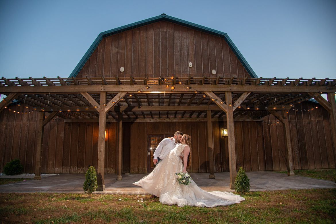 A bride and groom are kissing in front of a barn.