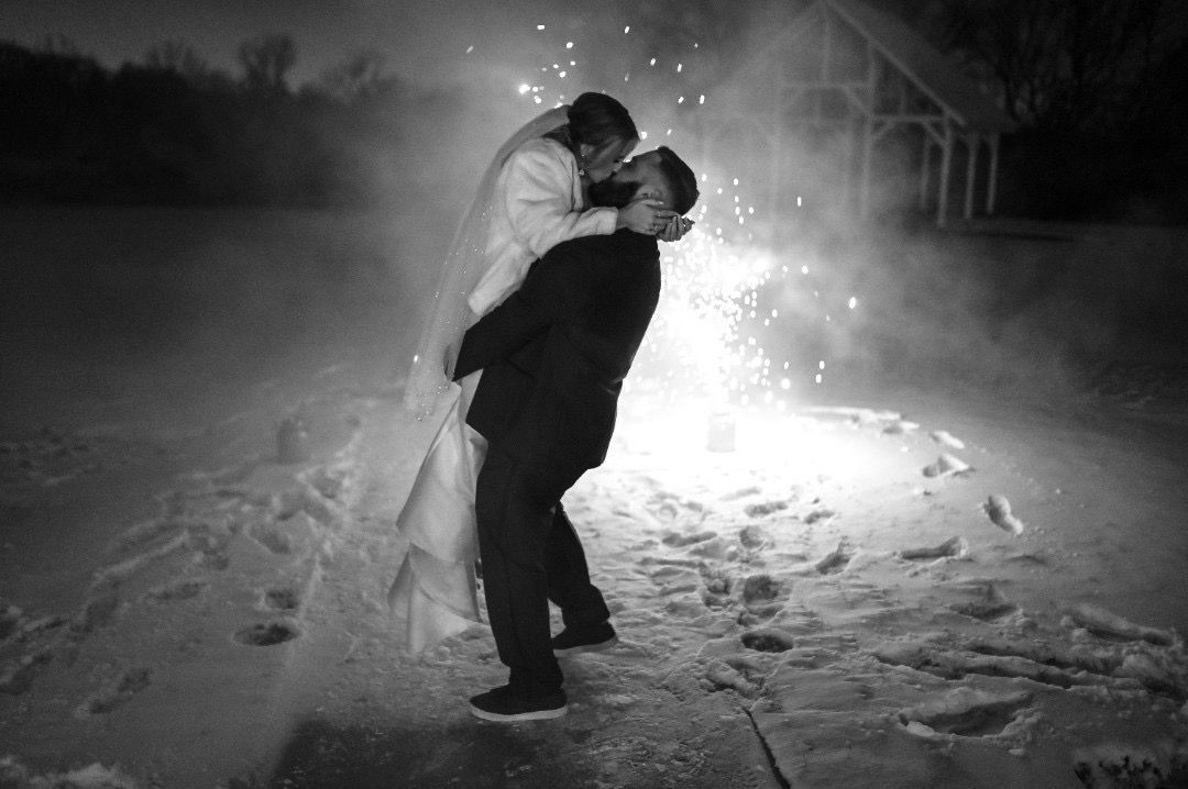 A bride and groom kissing in front of a fireworks display.