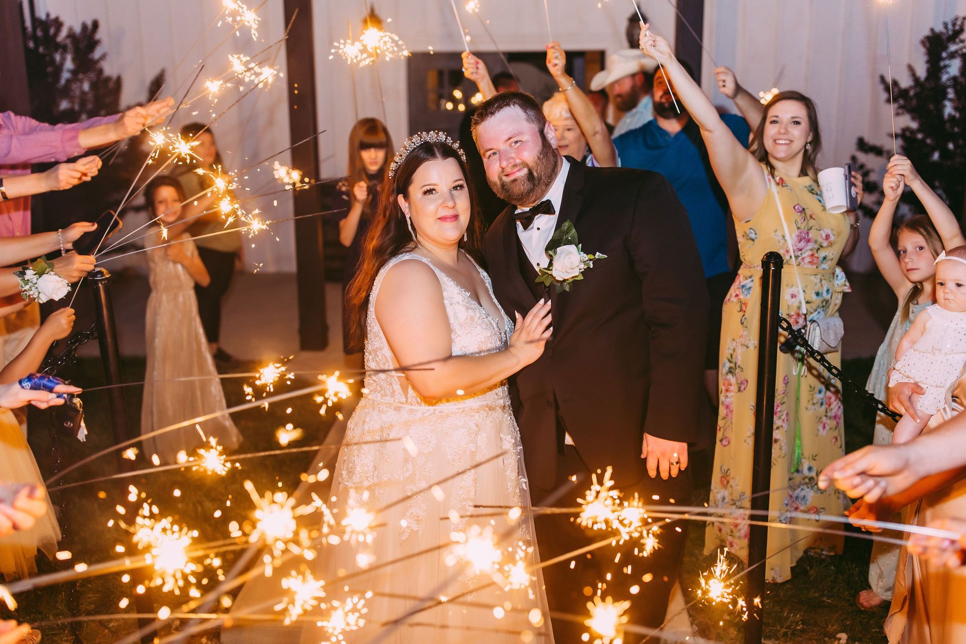 A bride and groom are standing in front of a crowd of people holding sparklers.