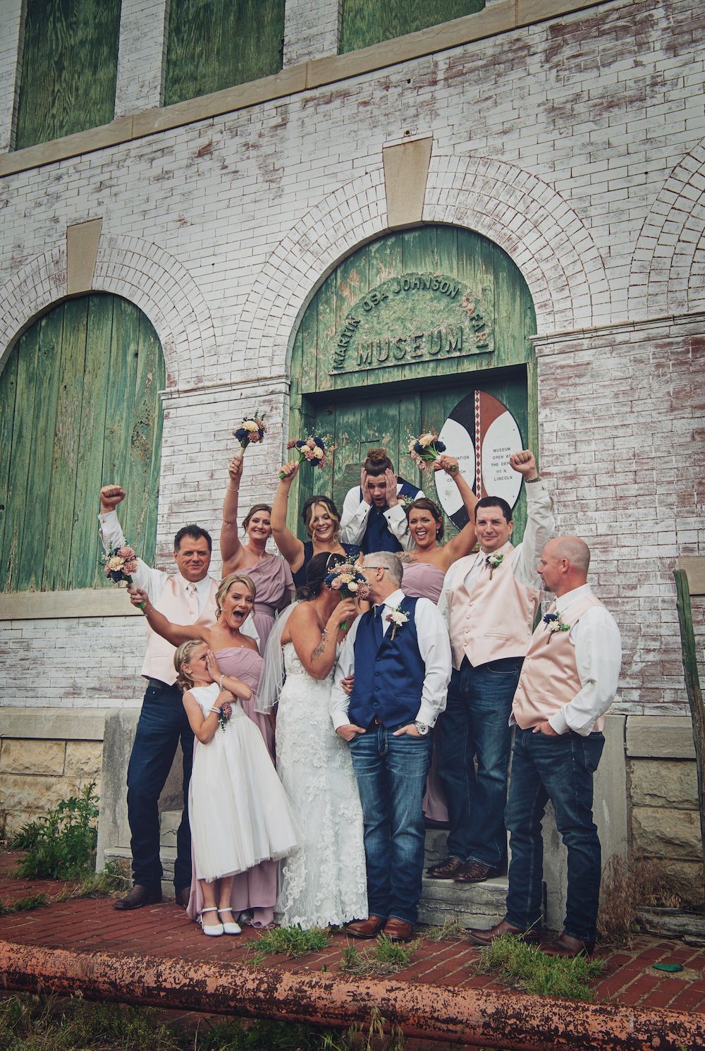 A wedding party is posing for a picture in front of a brick building.